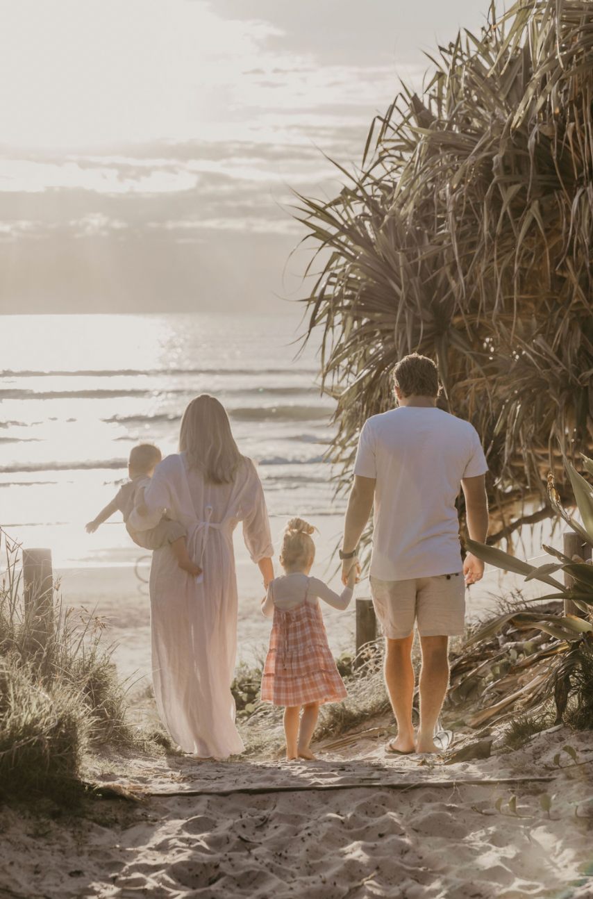 Family holding hand walking to beach down path in Byron Bay on sunrise.