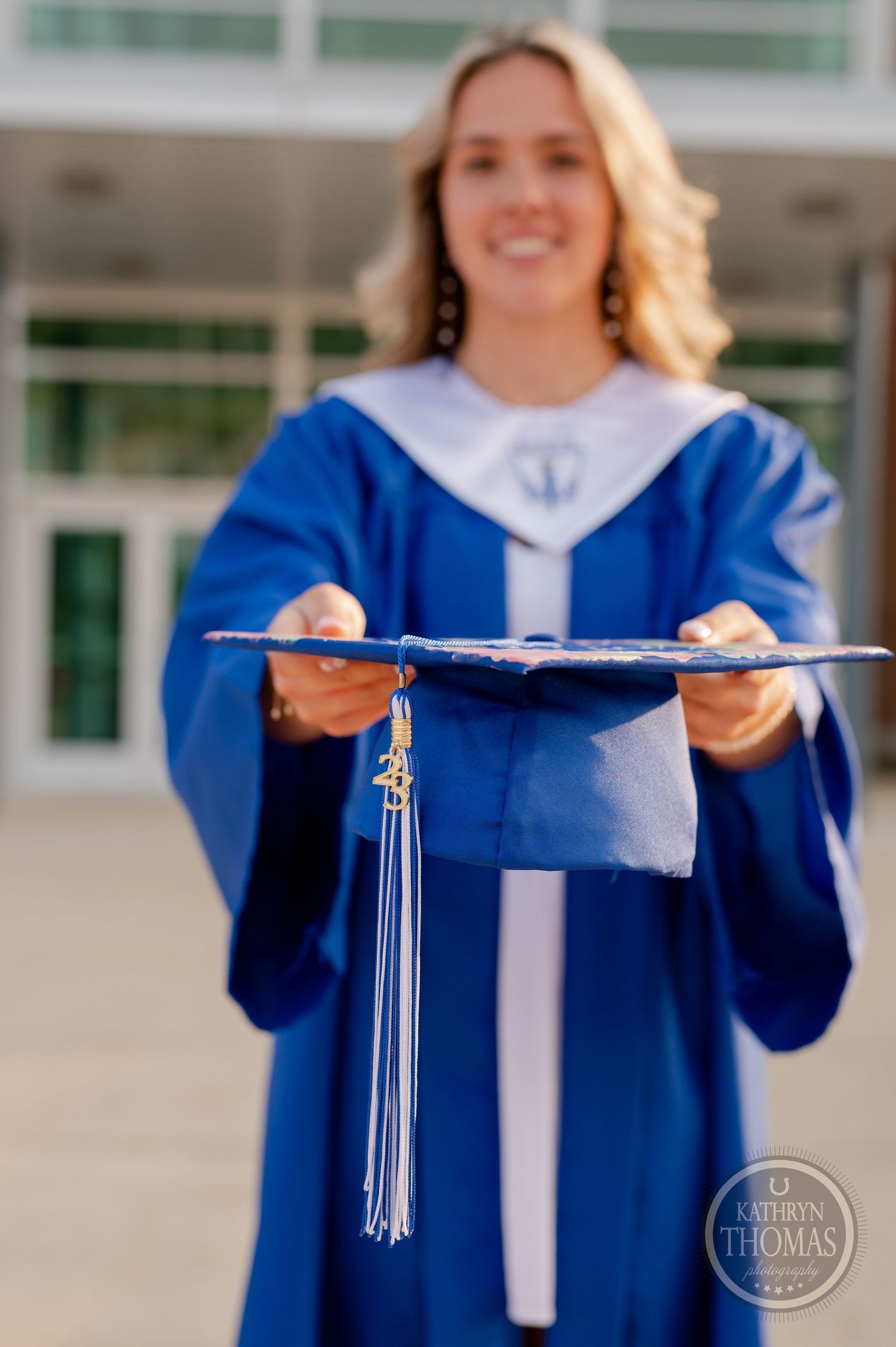 Graduate holding blue graduation cap with tassel in traditional ceremony attire.