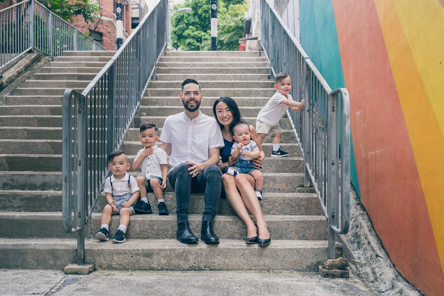 Family sitting together on colorful rainbow painted outdoor staircase.
