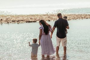 Family wading in shallow ocean water together during beach outing.