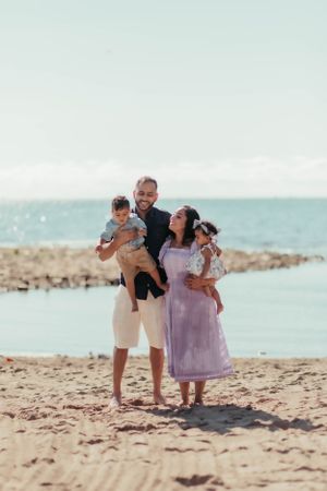 A family enjoys a sunny day together on a beach with turquoise waters in the background.