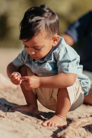 Young child in blue shirt and khaki shorts exploring sand at the beach.