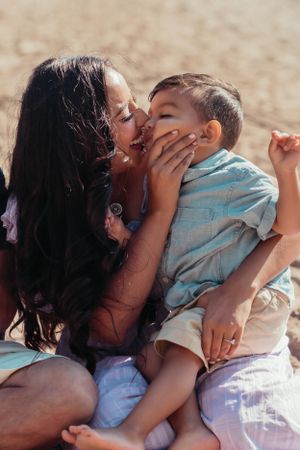 Tender moment between parent and child sitting on sandy beach.
