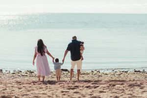 Family walking together hand in hand along shoreline during sunset at the beach.