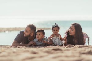 Family lying together on sandy beach with ocean view in background.
