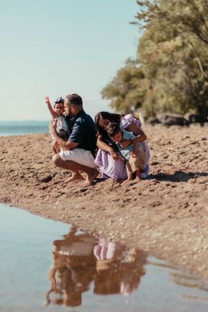 A scenic beach photo showing a family crouched down near the water's reflection.