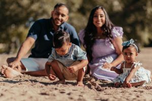 Family sitting together on sandy beach during outdoor photoshoot with natural lighting.