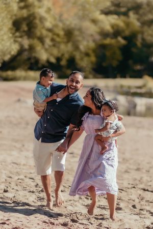 Happy family enjoying a playful moment together on a sunny beach with autumn foliage in the background.