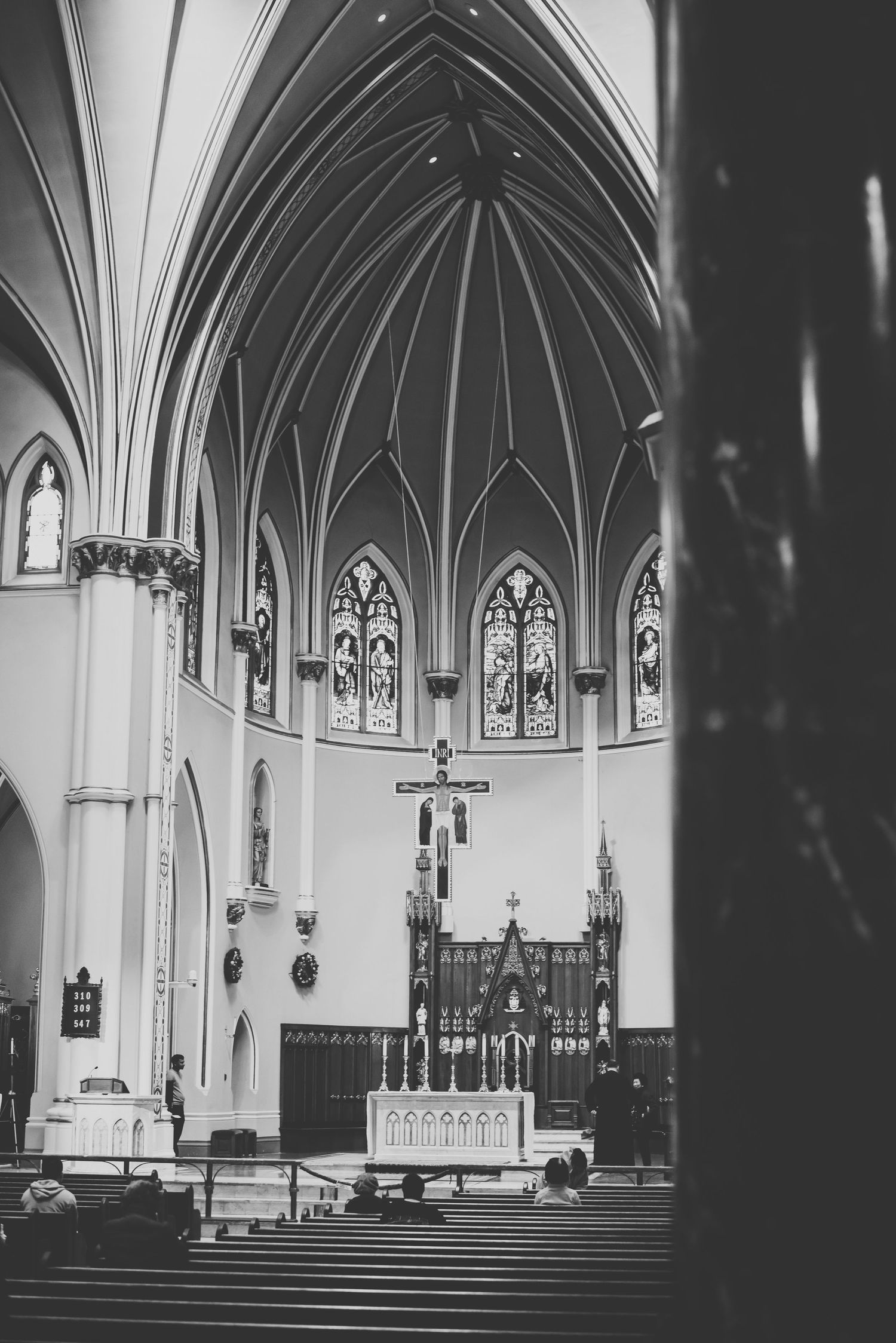 Black and white photograph of a church interior featuring gothic arches and stained glass windows.