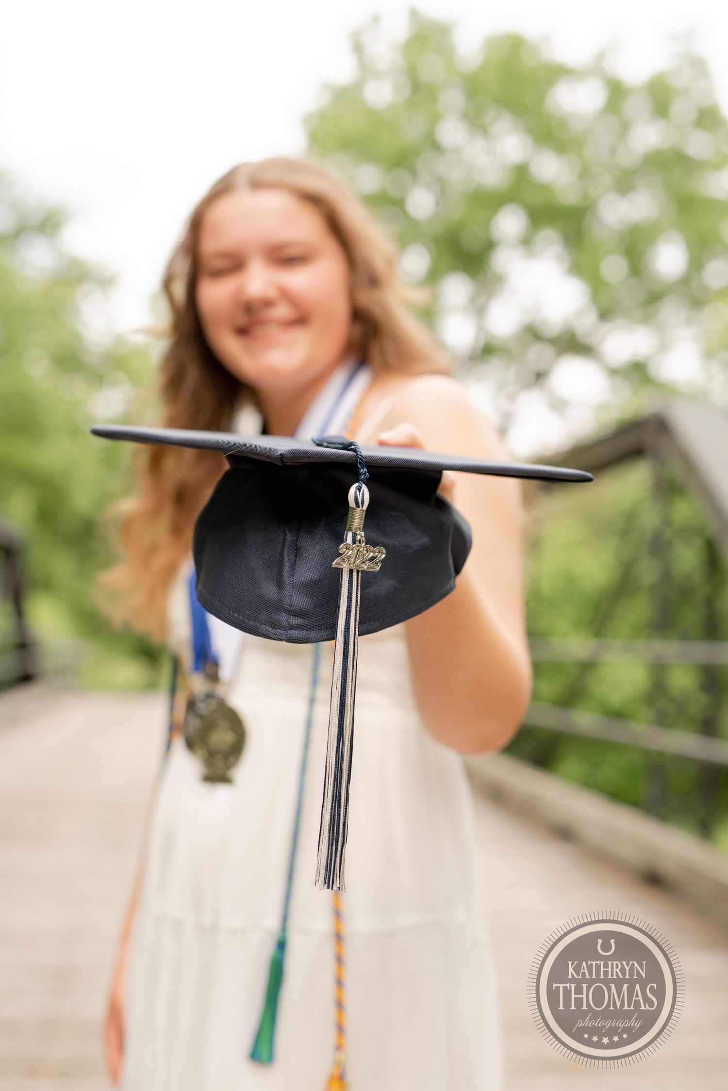 A graduation cap with tassel is held up on a wooden bridge.