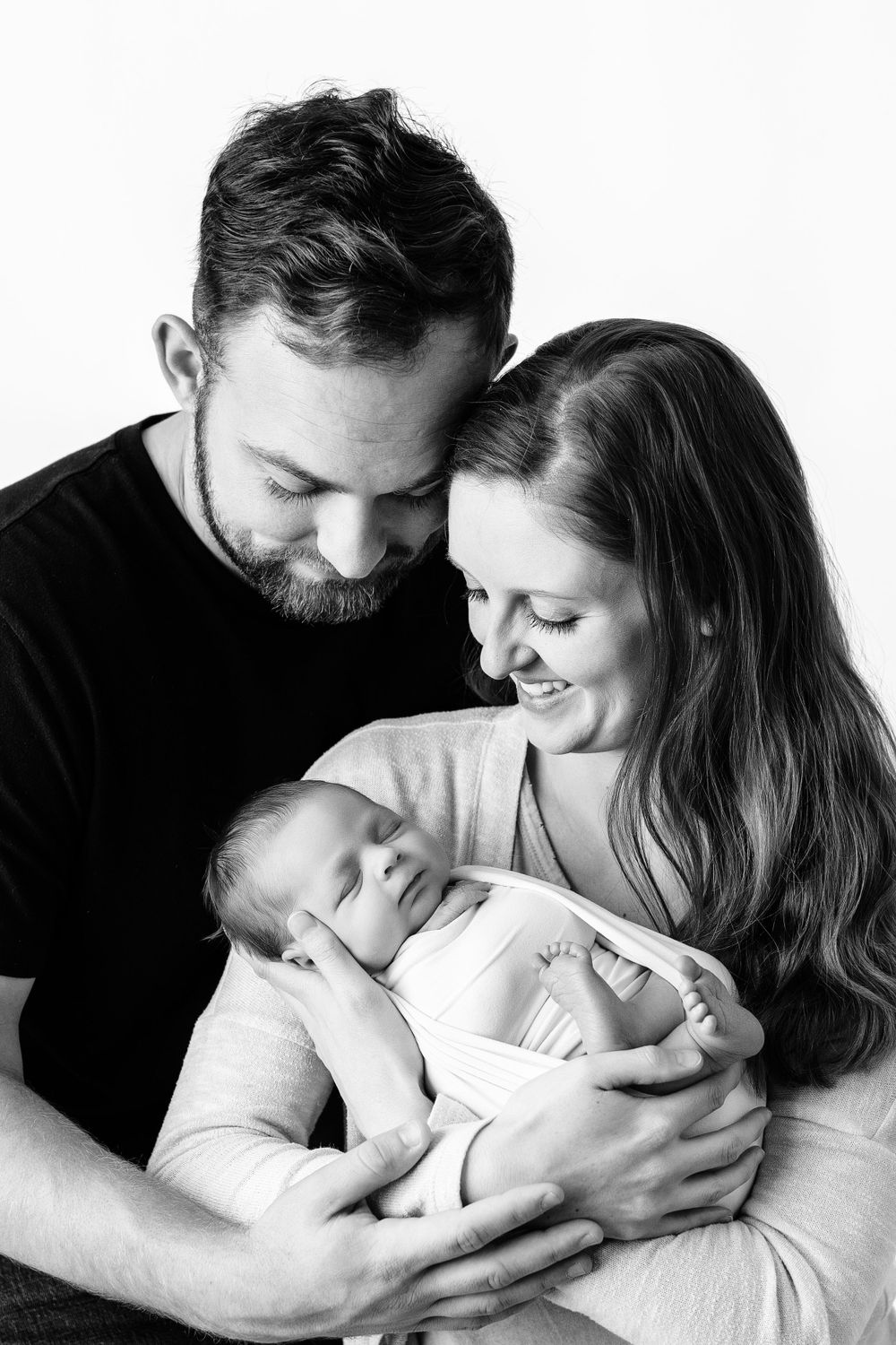 Black and white portrait of new parents tenderly holding their newborn baby against a white background.