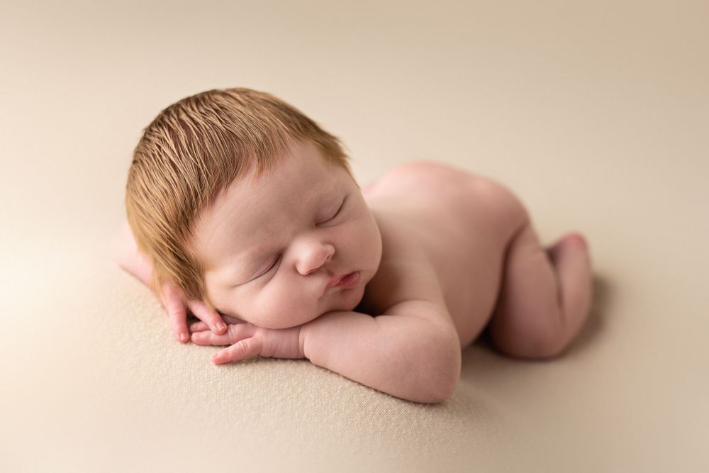 Sleeping newborn curled up on beige backdrop with peaceful expression.