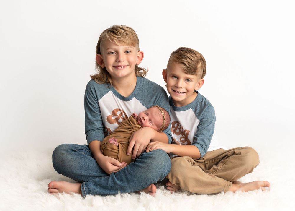 Two children in matching blue shirts sitting together holding a newborn baby.
