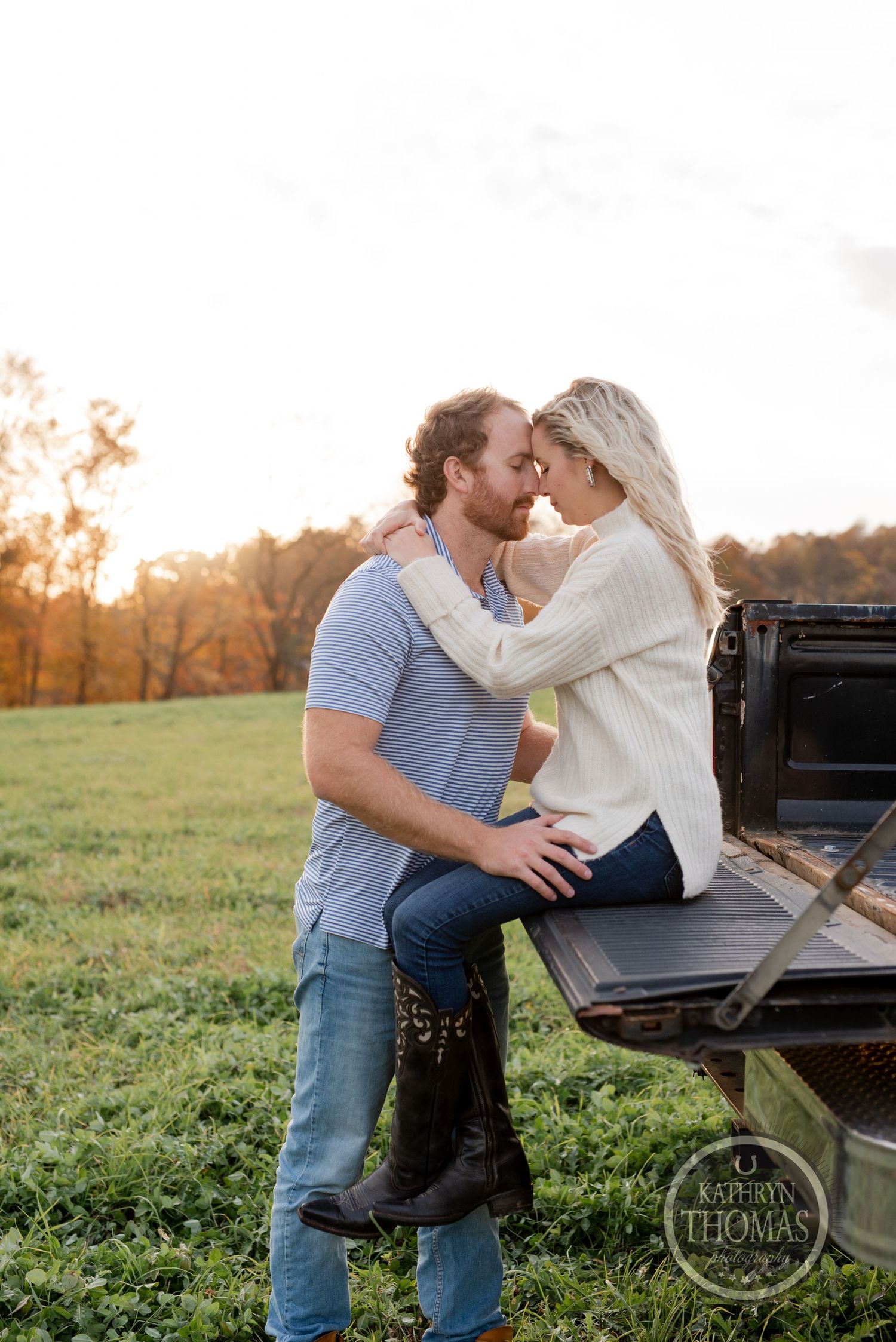 Intimate moment captured on truck tailgate during sunset with autumn colors in background.