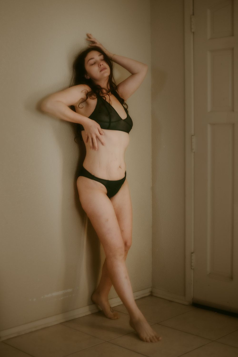 Artistic indoor portrait showcasing elegant poses in black swimwear against beige wall.