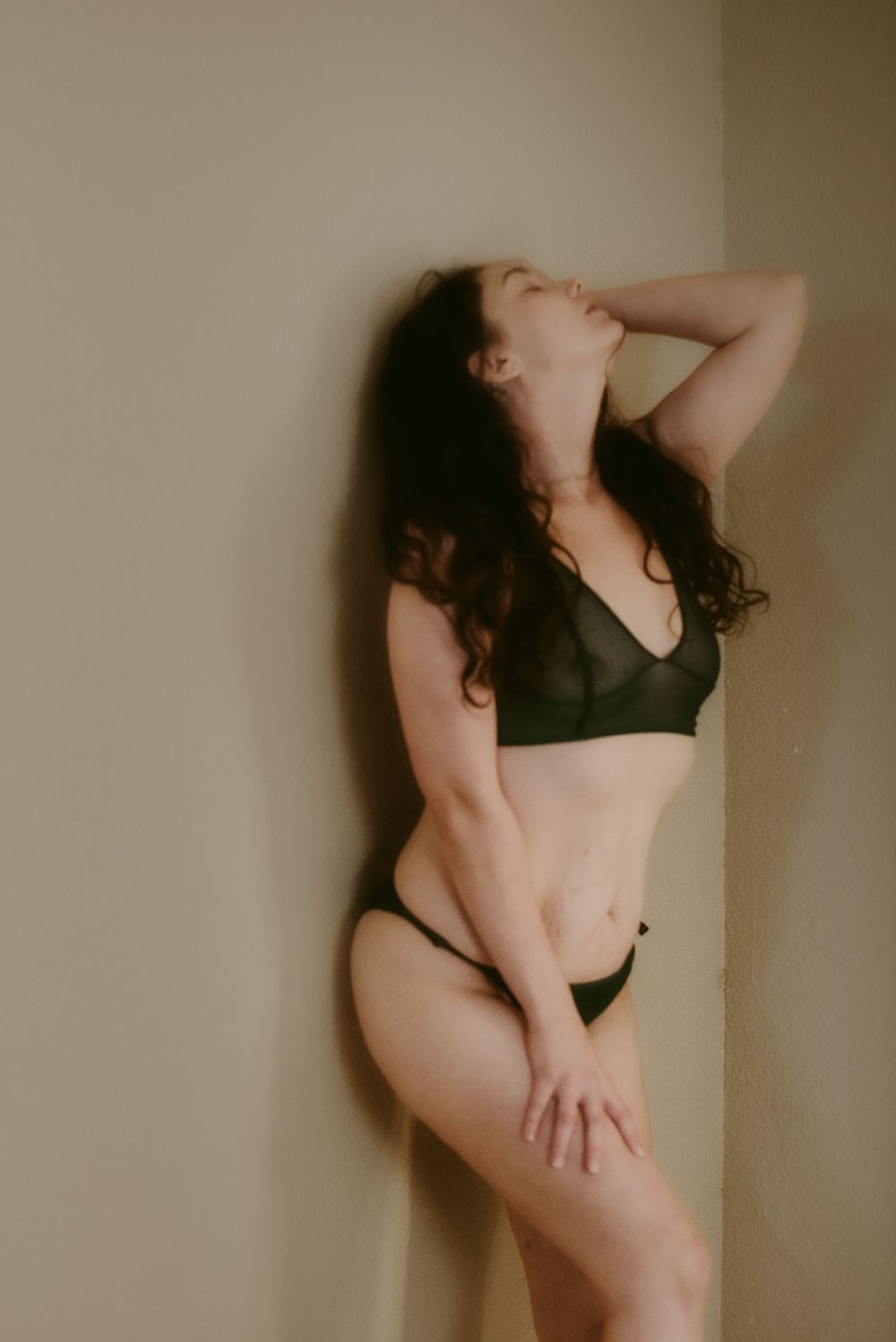 Intimate boudoir photo showing a figure in dark lingerie posing expressively.