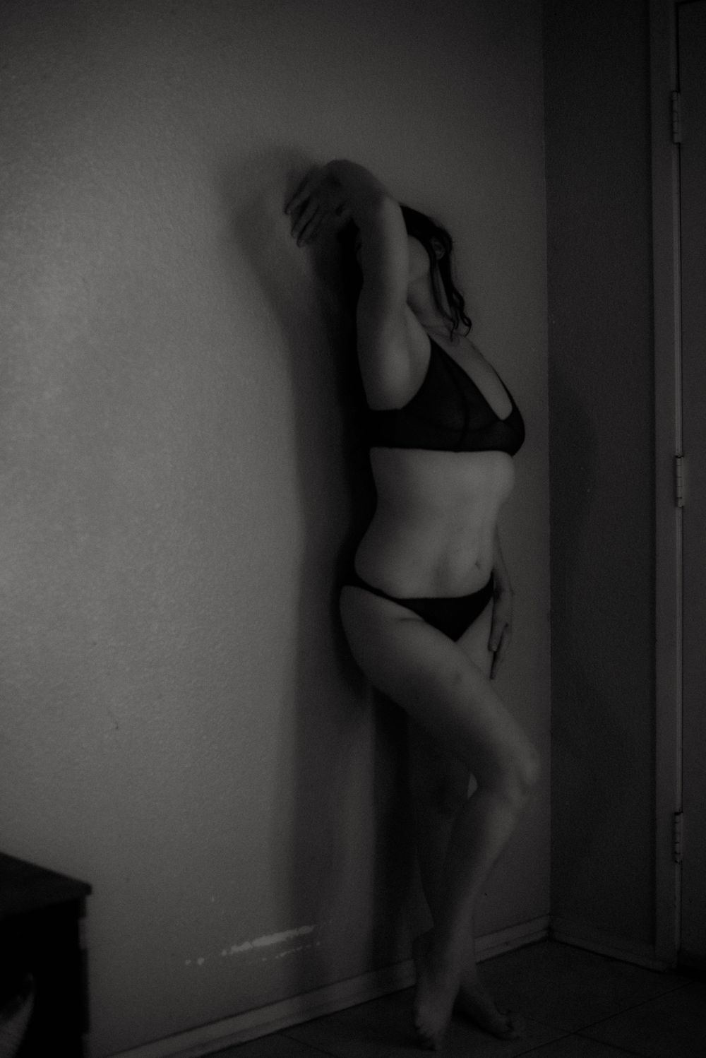 Moody black and white portrait of a silhouette in lingerie against a wall.