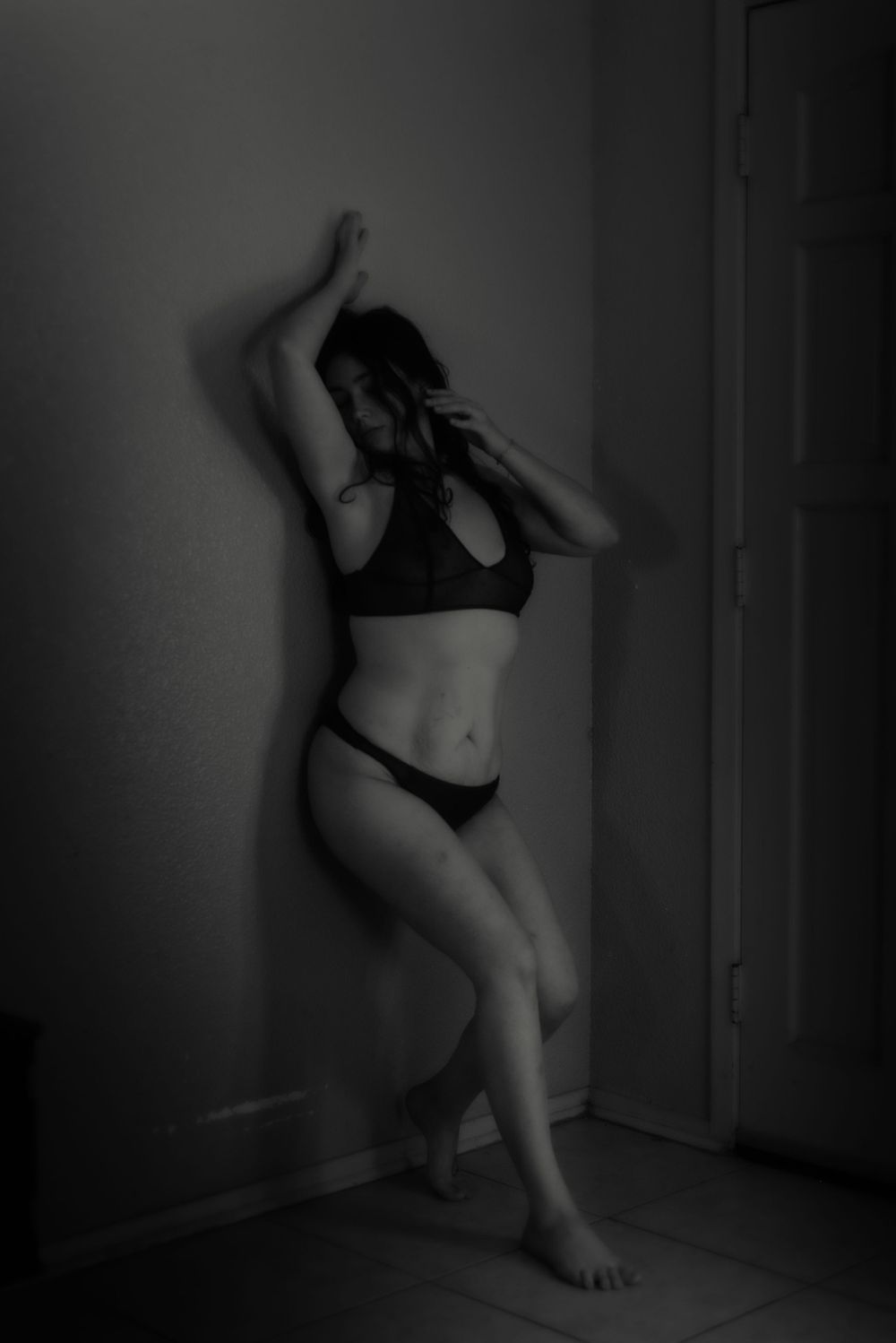 Dramatic black and white boudoir portrait showing artistic pose against wall.