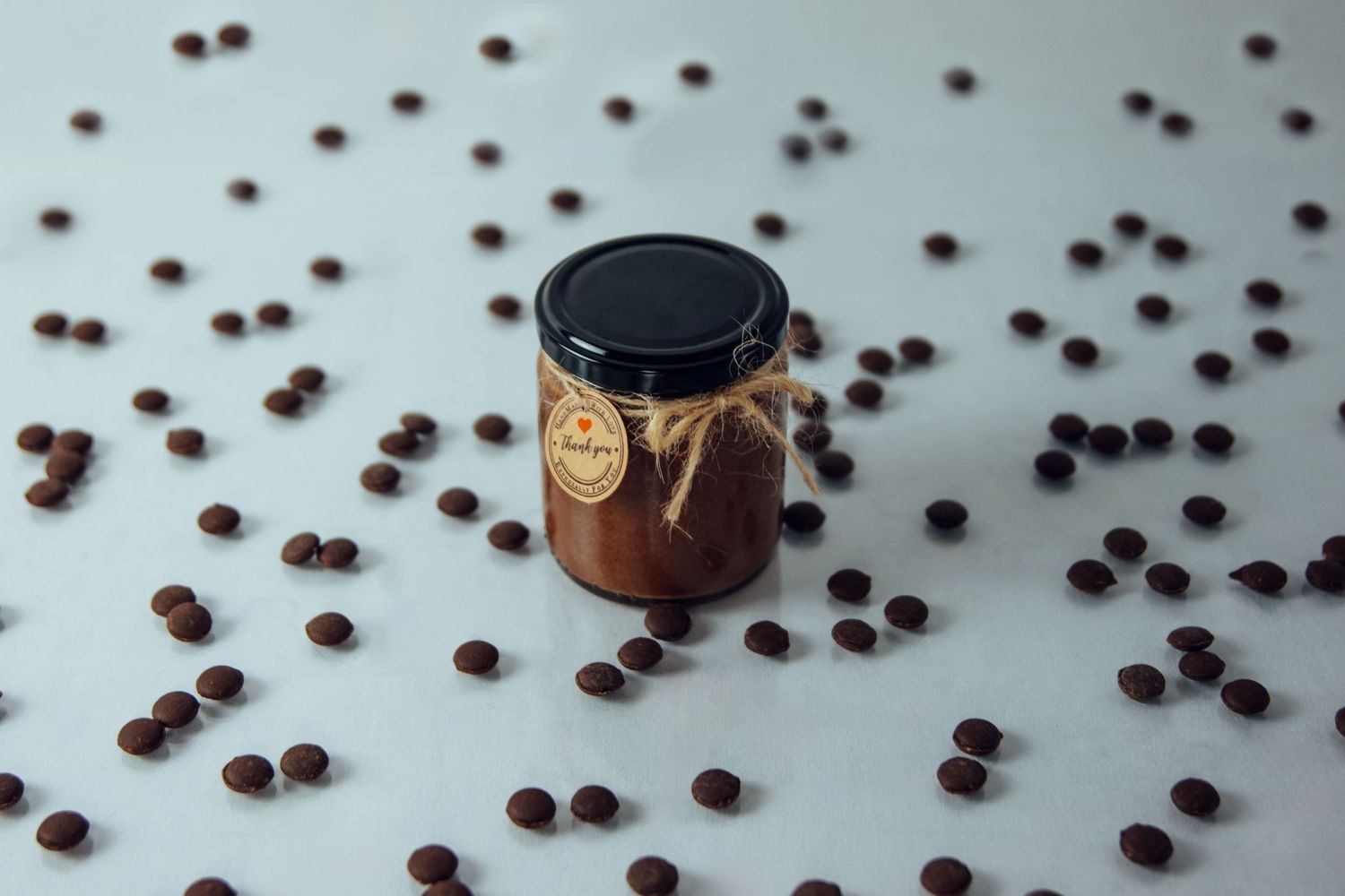Coffee beans scattered across light blue surface with glass jar in frame.