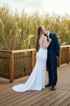 Romantic wedding photo of couple embracing on wooden boardwalk surrounded by nature.