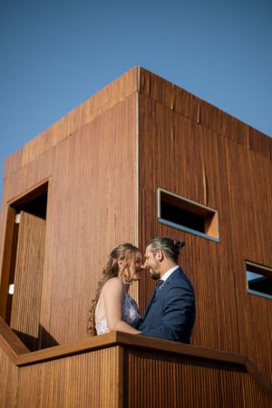 Couple sharing an intimate moment on a wooden balcony against modern architecture.