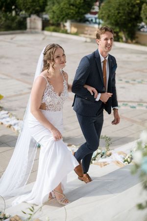 Bride in lace gown and groom in pinstripe suit walking up decorated church steps.
