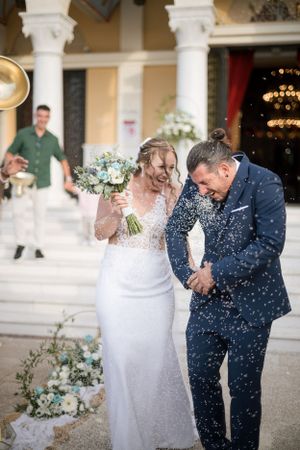Joyful wedding couple showered with confetti on grand columned steps.