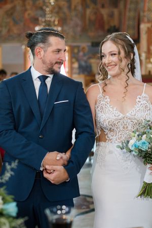 Joyful wedding couple during ceremony in ornately decorated church with painted walls.