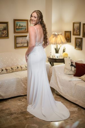 Elegant bride in fitted white wedding gown poses in a beautifully decorated room.