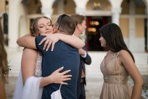 Emotional group hug during wedding celebration outside columned building.