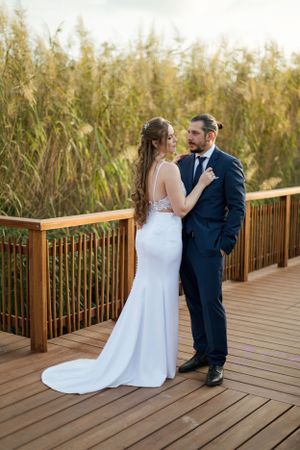 Wedding couple poses on wooden boardwalk with tall grass in background.