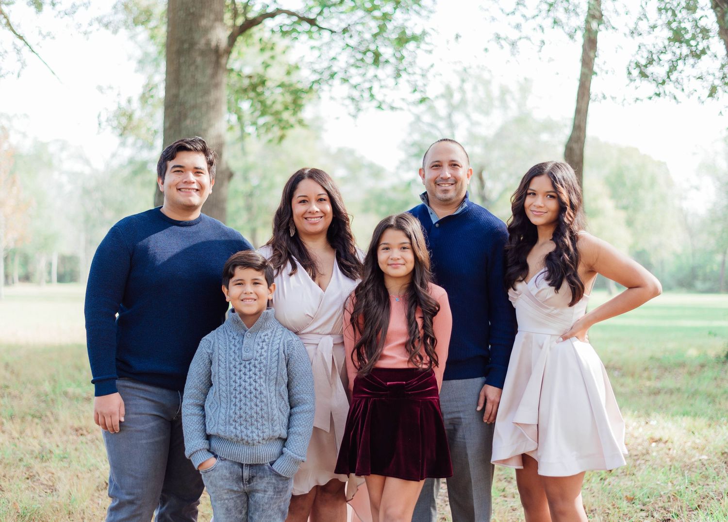 Family wearing coordinated casual outfits poses together in a natural outdoor setting.
