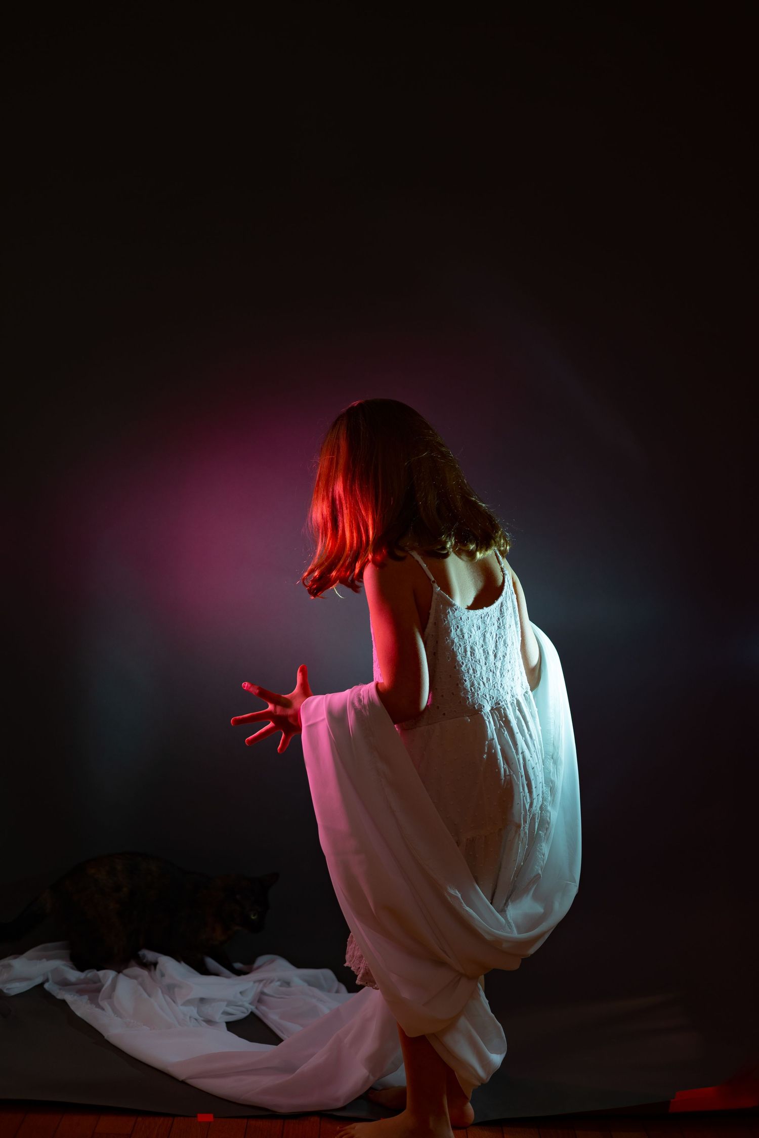 Artistic portrait of a figure in flowing white dress illuminated by colorful lighting effects.