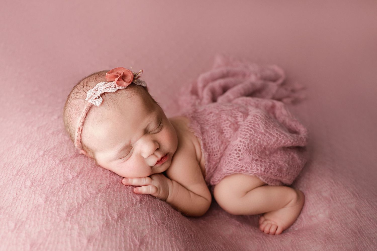 Fine art newborn portrait of baby girl in pink lying on her side with flowing fabric