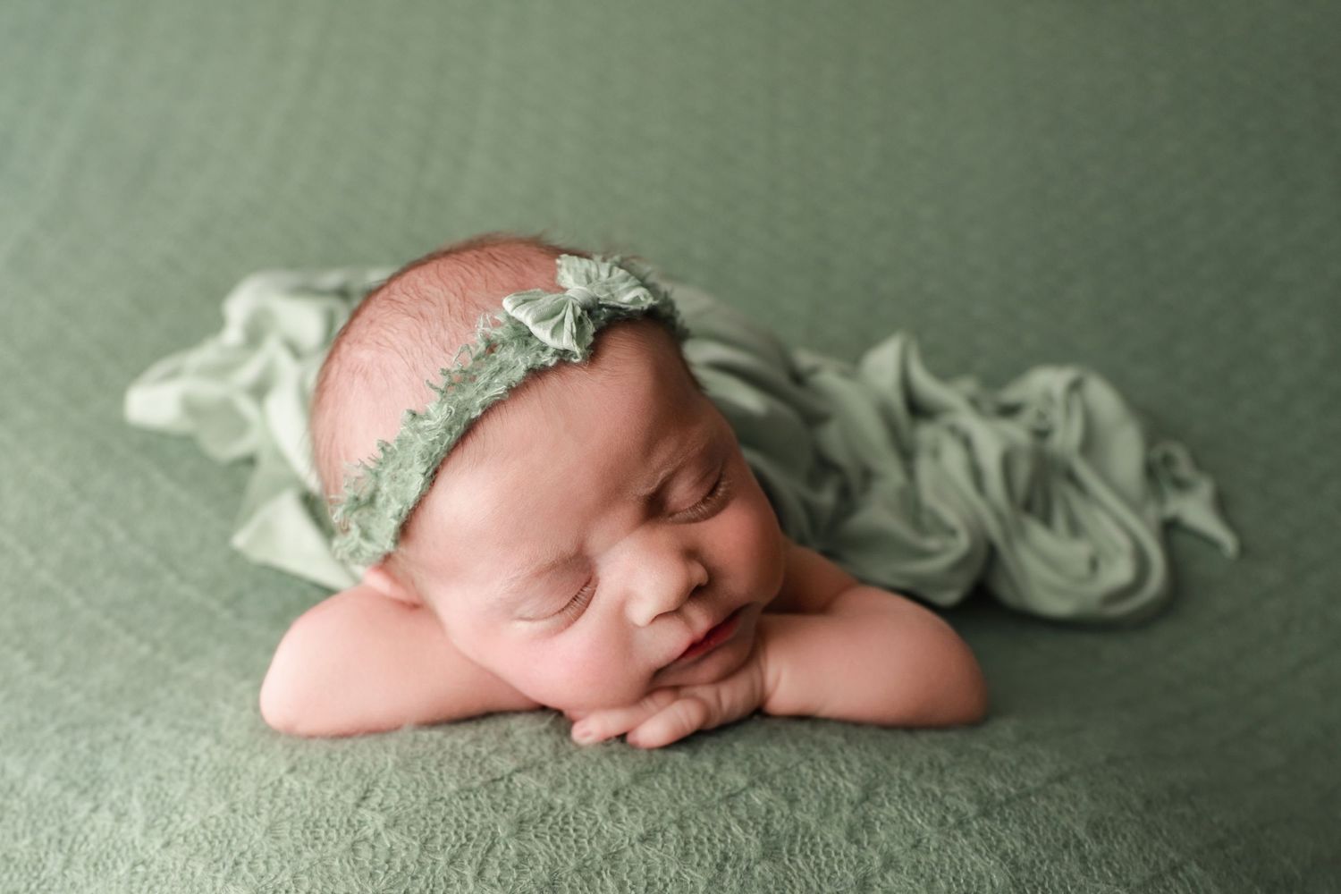 Fine art newborn portrait of baby girl with chin on hands in green