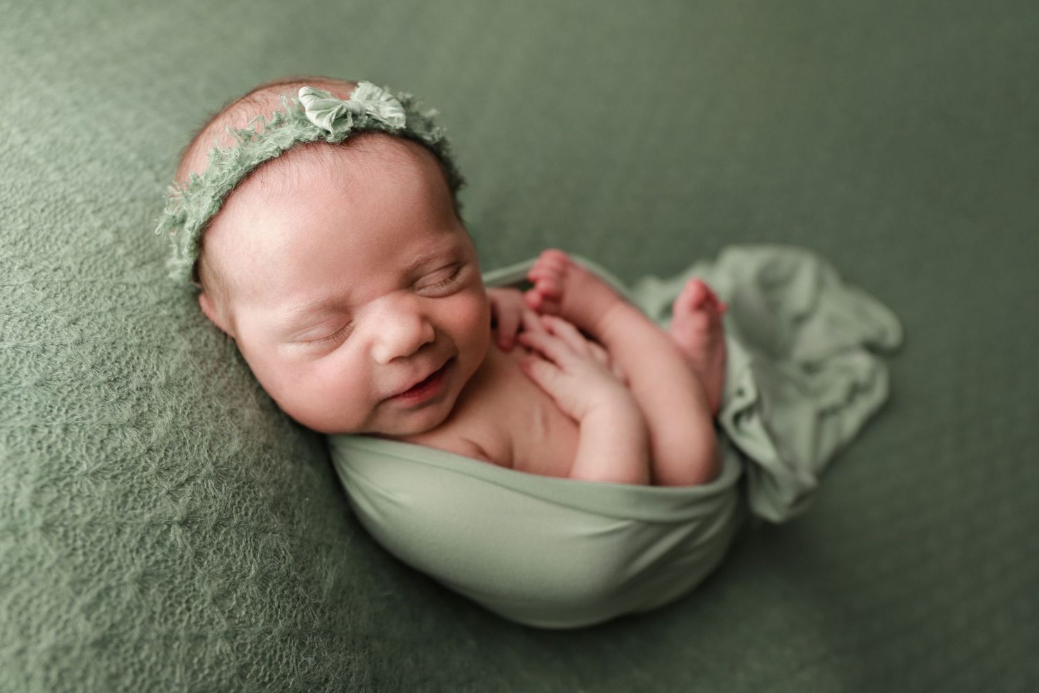 Fine art newborn portrait of baby girl with headband in green smiling