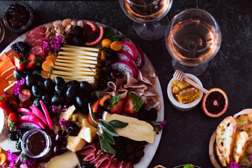 Overhead view of a charcuterie board with meats, cheeses, grapes and two glasses of rosé wine for winery and catering branding photography.