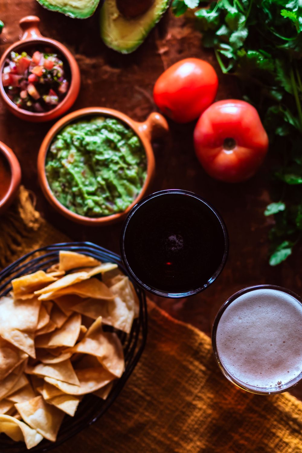 Overhead view of fresh guacamole, tomatoes, chips and beverages for Mexican appetizers for restaurant branding photography.