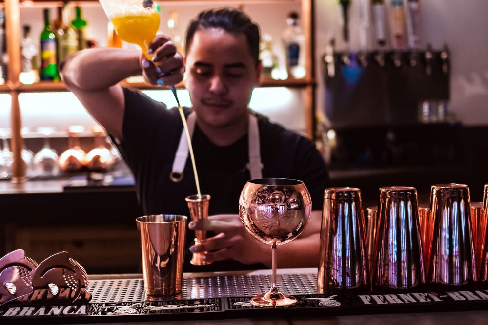 Mixologist crafting cocktails at a well-stocked bar with colorful bottles for restaurant branding photography.
