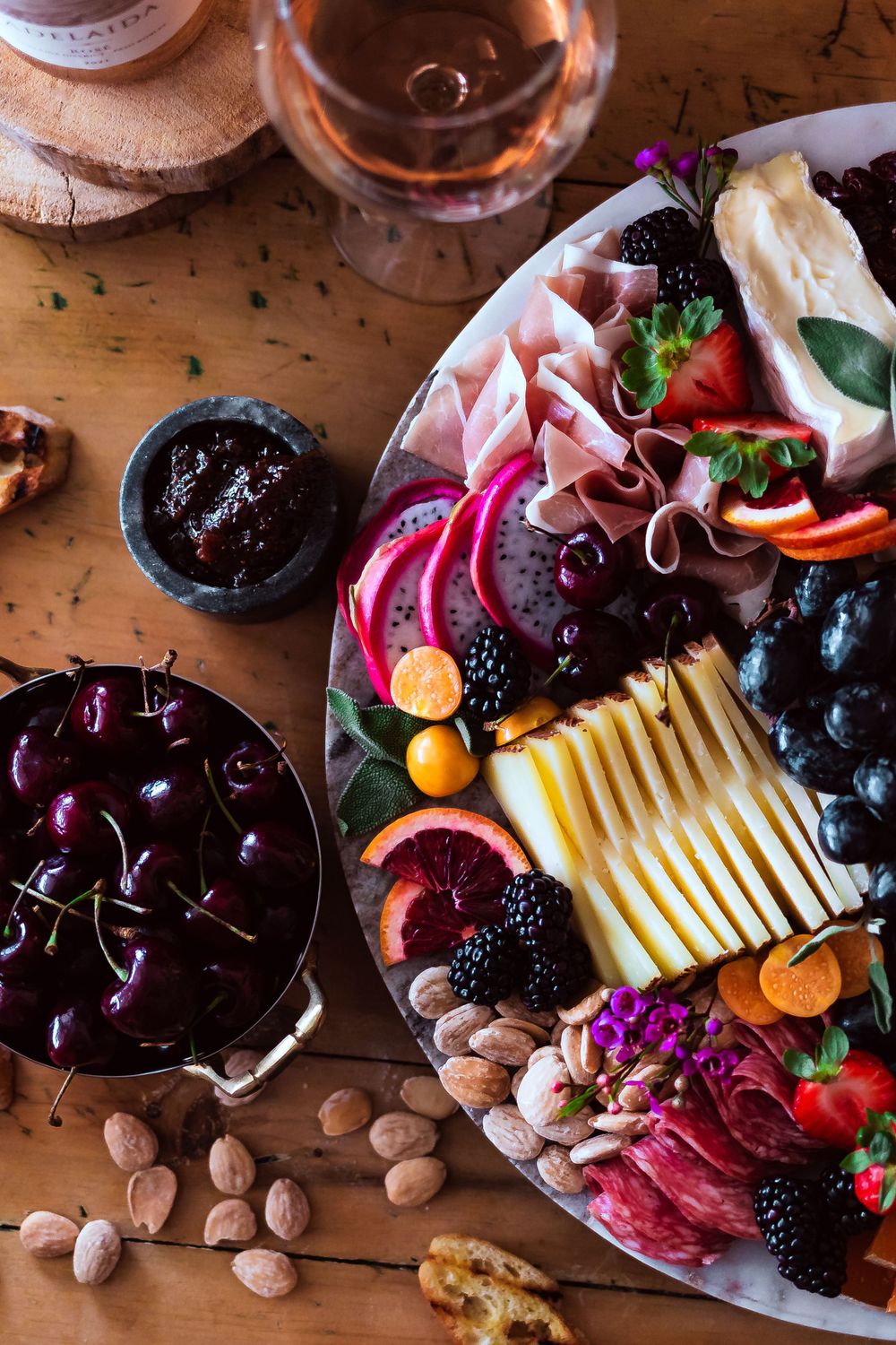 Artisanal cheese board with cured meats, fresh fruits, nuts and wine on wooden surface for winery and catering branding photography.