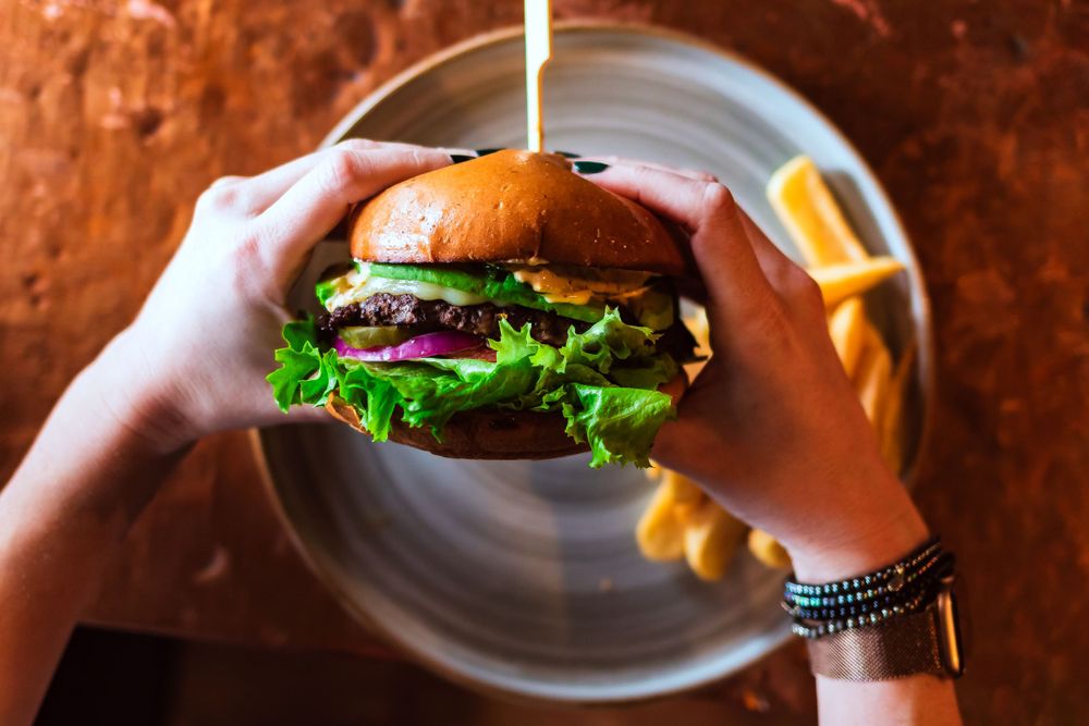 Hands holding a juicy cheeseburger with fresh lettuce and tomato on a white plate for restaurant branding photography.