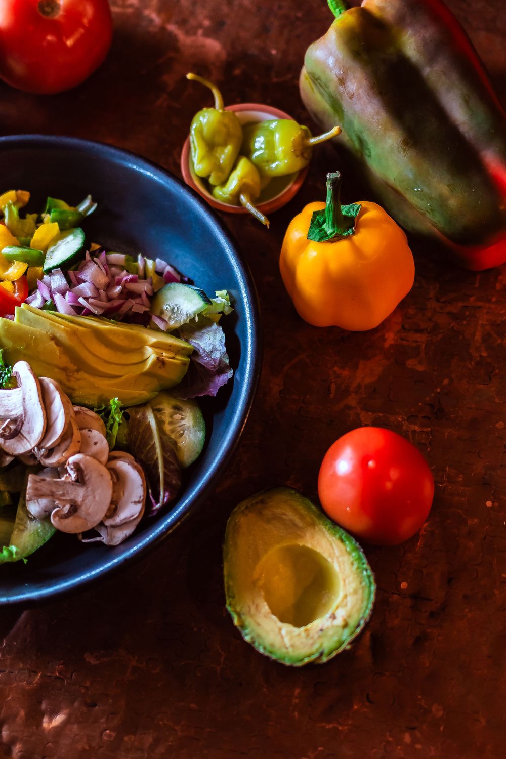 Fresh ingredients including avocado, tomatoes, and bell peppers around a prepared salad bowl for restaurant branding photography.
