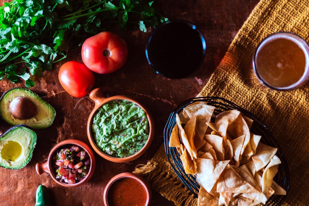 Fresh ingredients for Mexican cuisine including guacamole, salsa, tomatoes and tortilla chips on wooden surface for restaurant branding phot