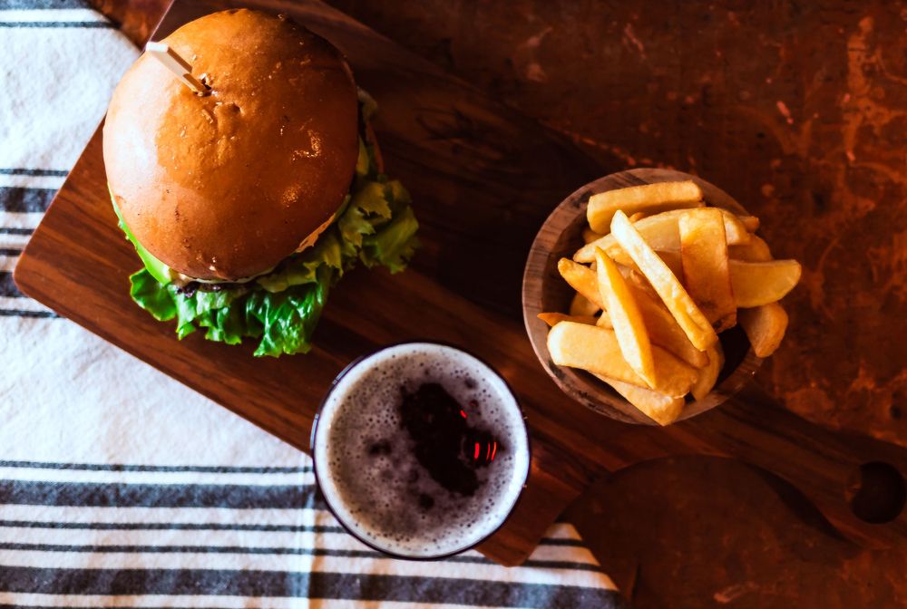 Classic cheeseburger on wooden board with side of french fries and dark beer for restaurant branding photography.