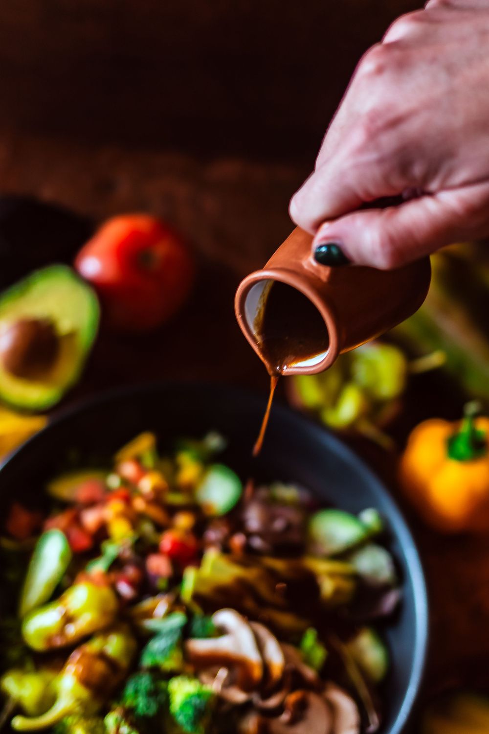 Close-up of sauce being poured over a vibrant salad bowl with fresh vegetables and mushrooms for restaurant branding photography.