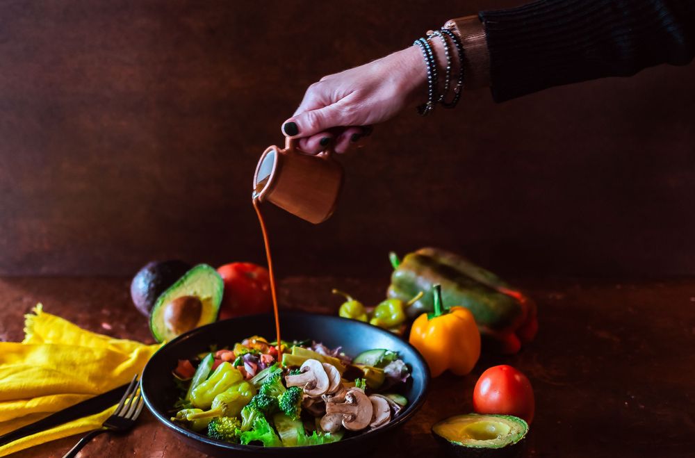 Pouring sauce over a colorful bowl of fresh vegetables and avocado for restaurant branding photography.