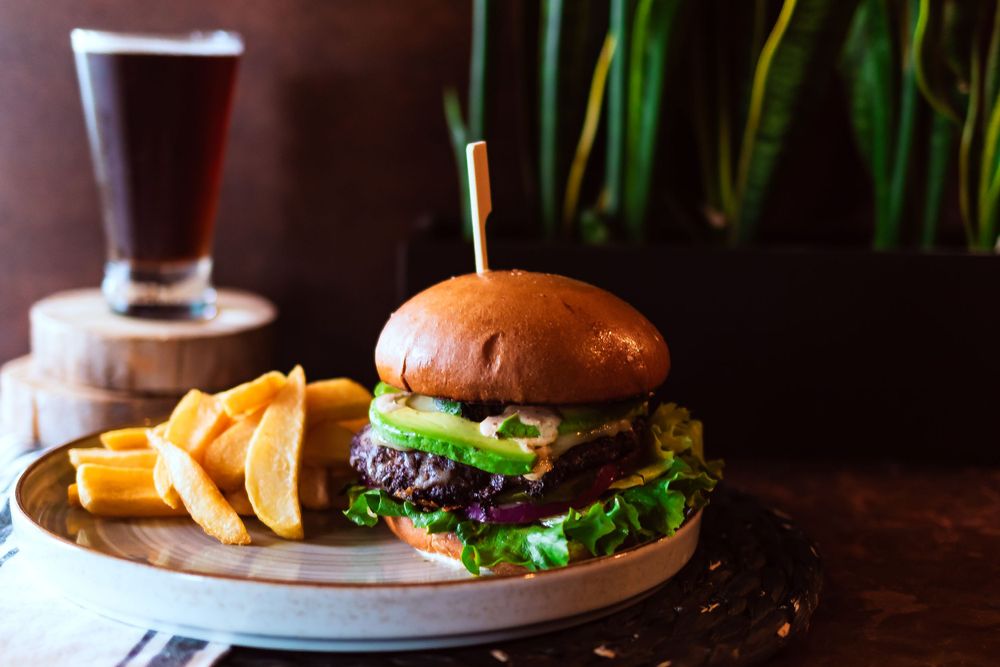 Gourmet burger with lettuce on brioche bun served with french fries and dark beer for for winery and catering branding photography.