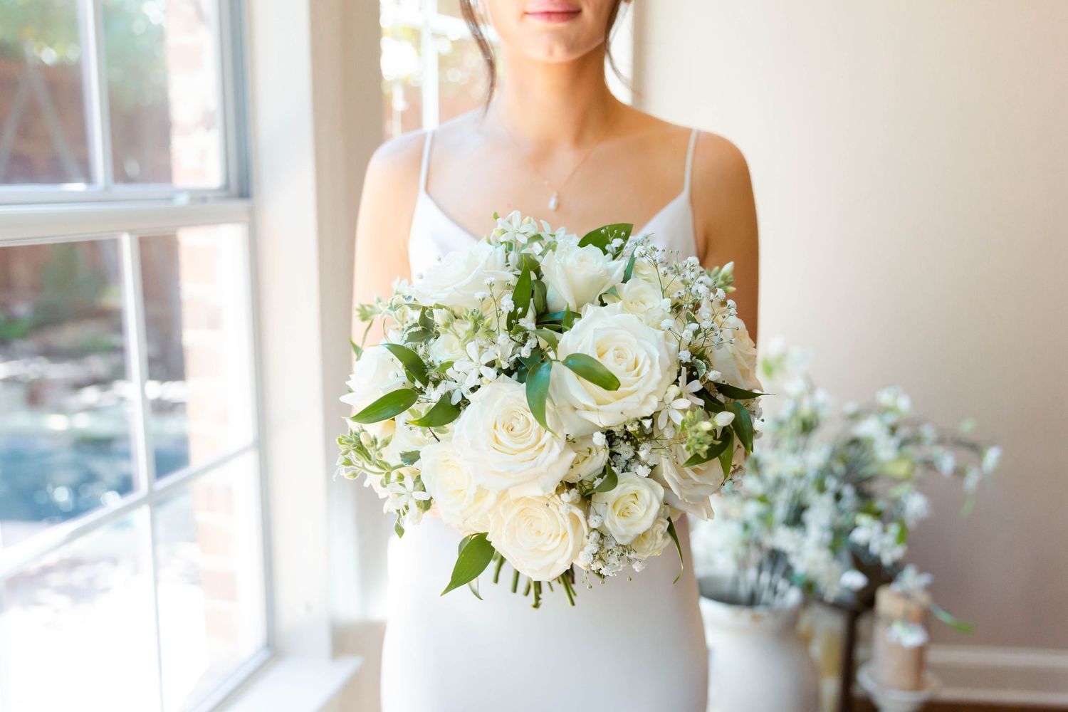 A classic bridal portrait featuring a white floral bouquet by a window.