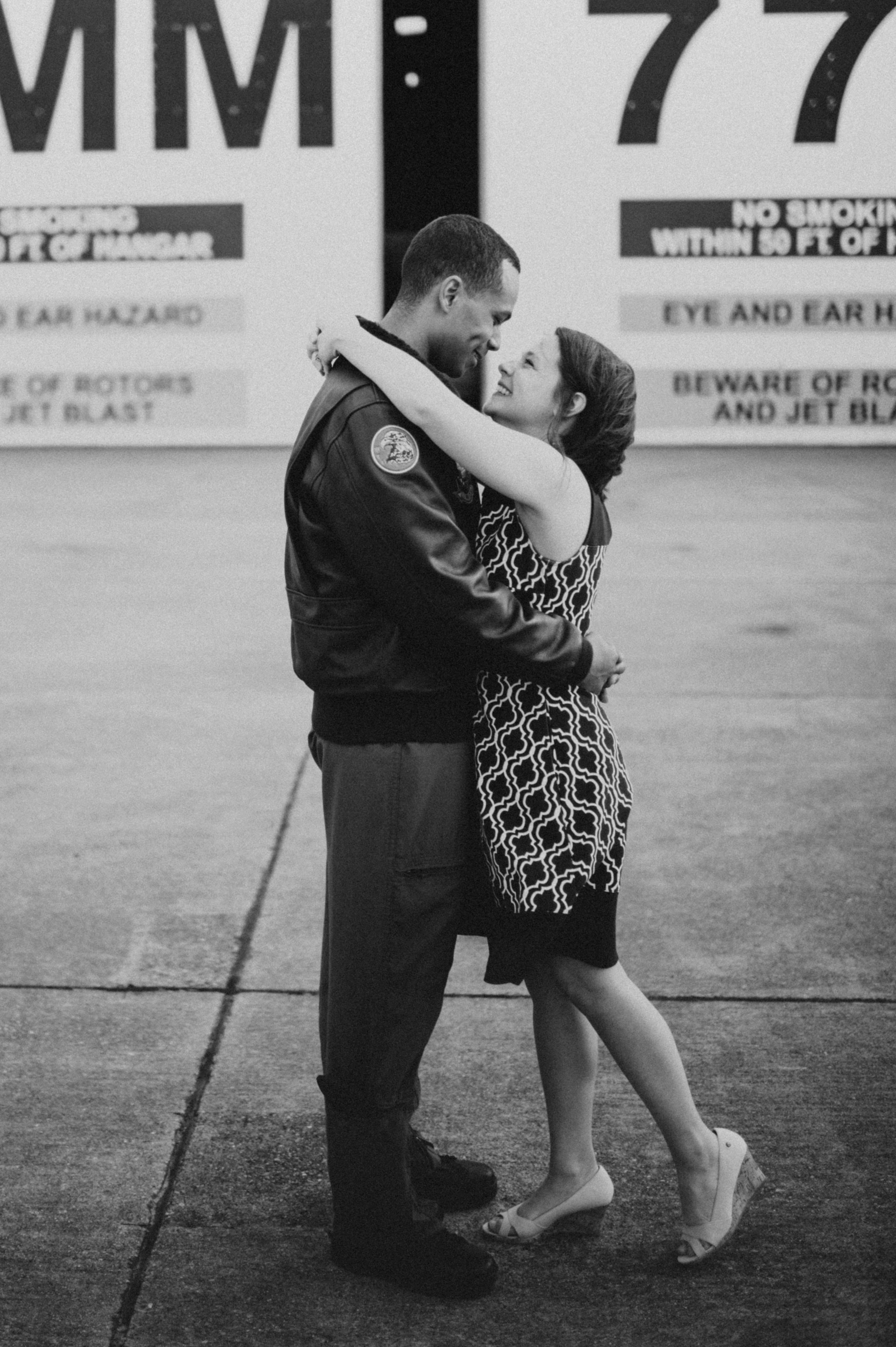 Intimate black and white portrait of couple embracing by military hangar.