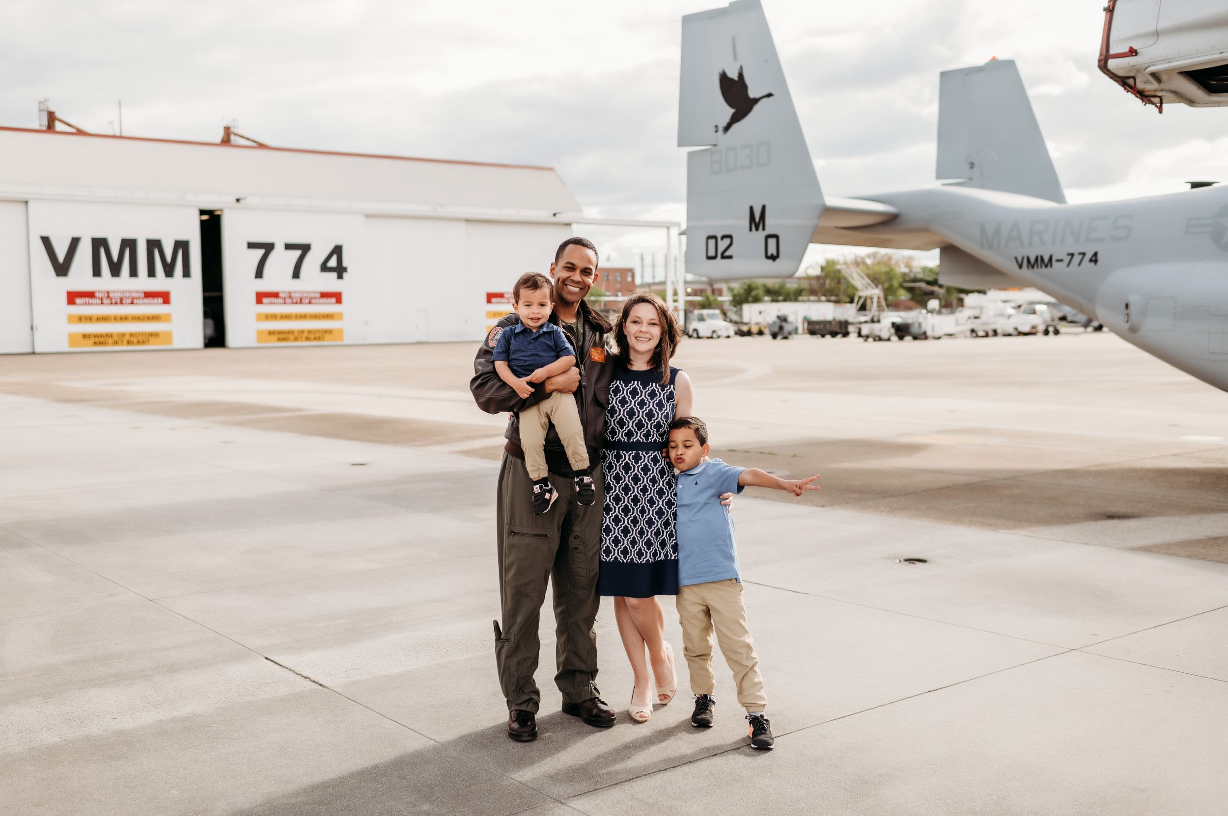 Family portrait on airfield tarmac with military aircraft tail visible.